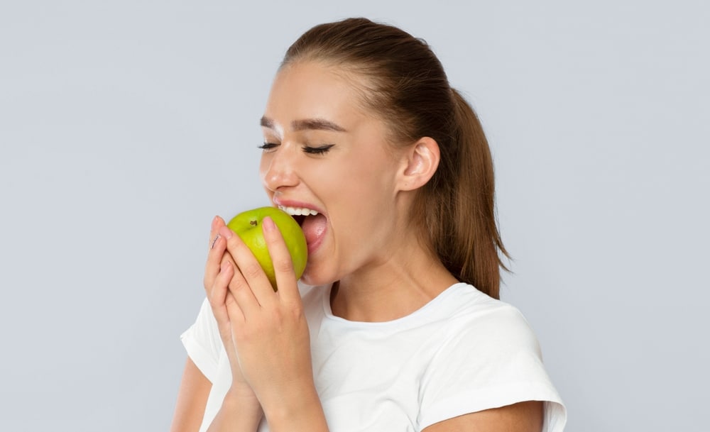 Young,Lady,Biting,Green,Apple,Standing,Over,White,Background.,Healthy