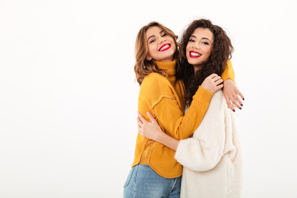Two,Pleased,Girls,In,Sweaters,Hugging,To,Each,Other,And