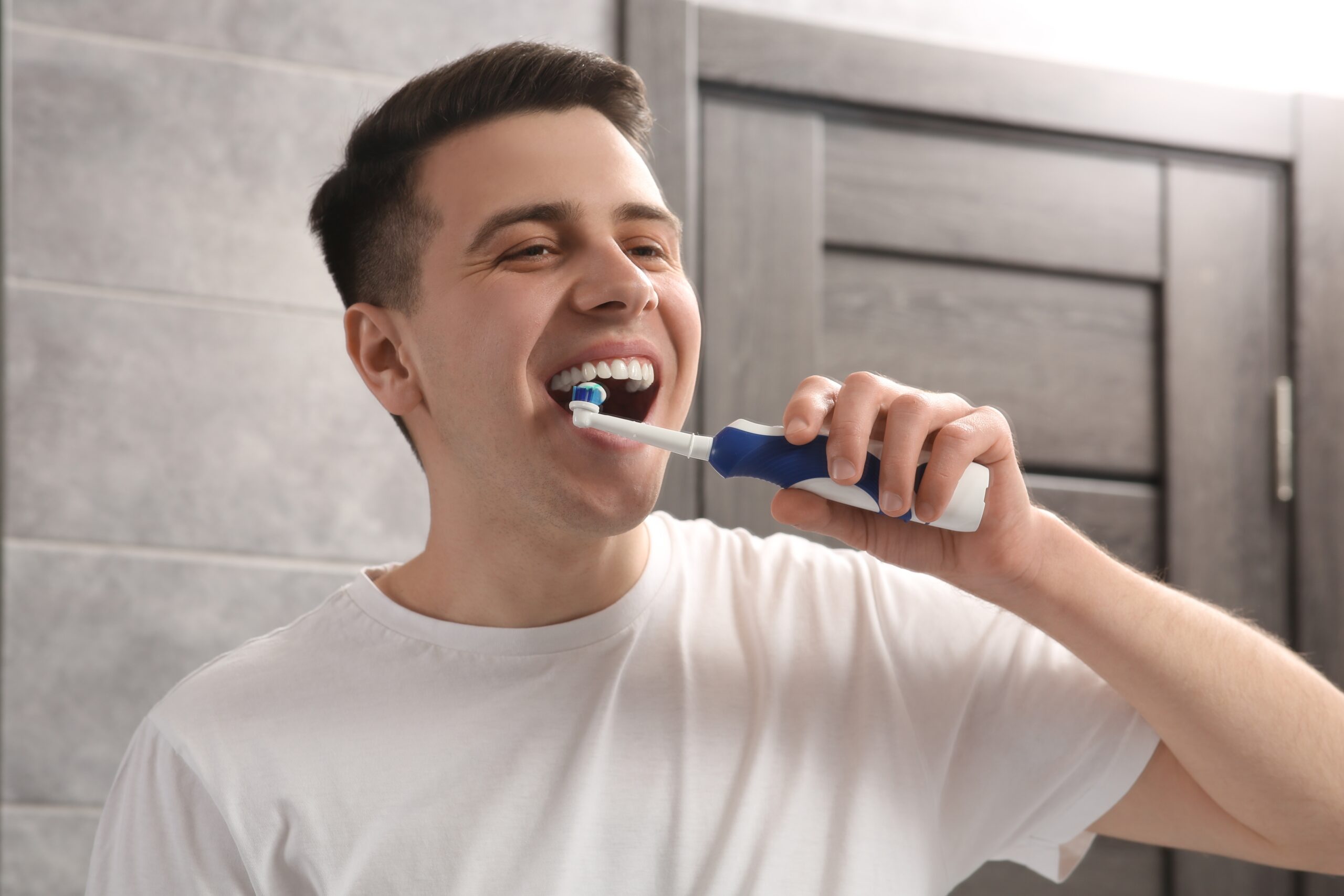 Man,Brushing,His,Teeth,With,Electric,Toothbrush,In,Bathroom